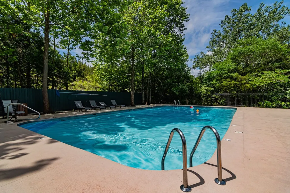 This image showcases a sparkling outdoor swimming pool surrounded by lounge chairs and lush trees. The clear blue water and relaxing atmosphere invite both swimming and sunbathing, while the tranquil setting hints at a resort-like escape for families.