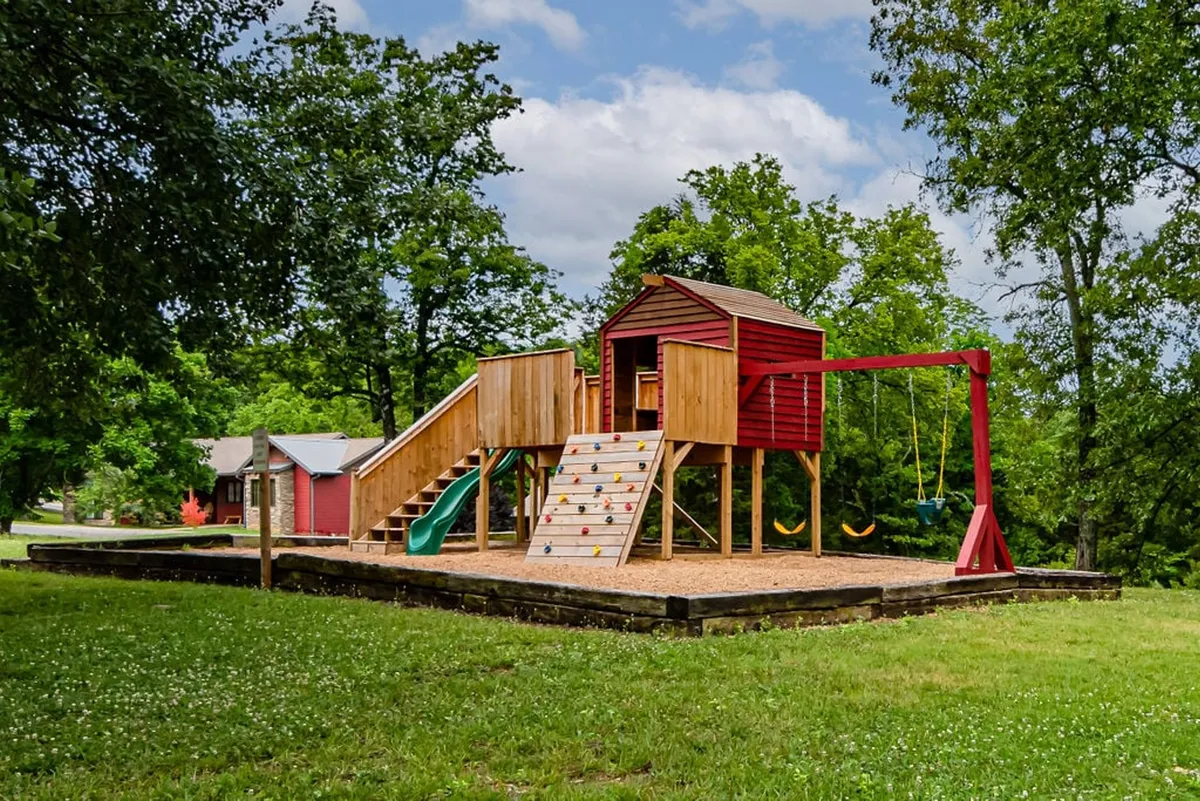 A vibrant playground structure with swings and a climbing wall sits surrounded by greenery, buzzing with children playing and families gathering. The joyful scene emphasizes active fun and togetherness in the community.