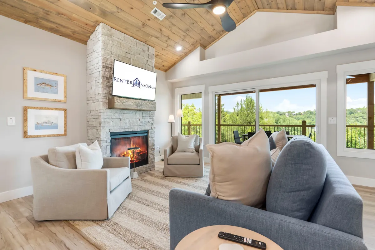 A comfortable living space with a stone fireplace, large windows, and plush seating options. A TV is mounted in the background, offering options for family movie nights or game days. The space feels both stylish and inviting, encouraging relaxation and group activities.