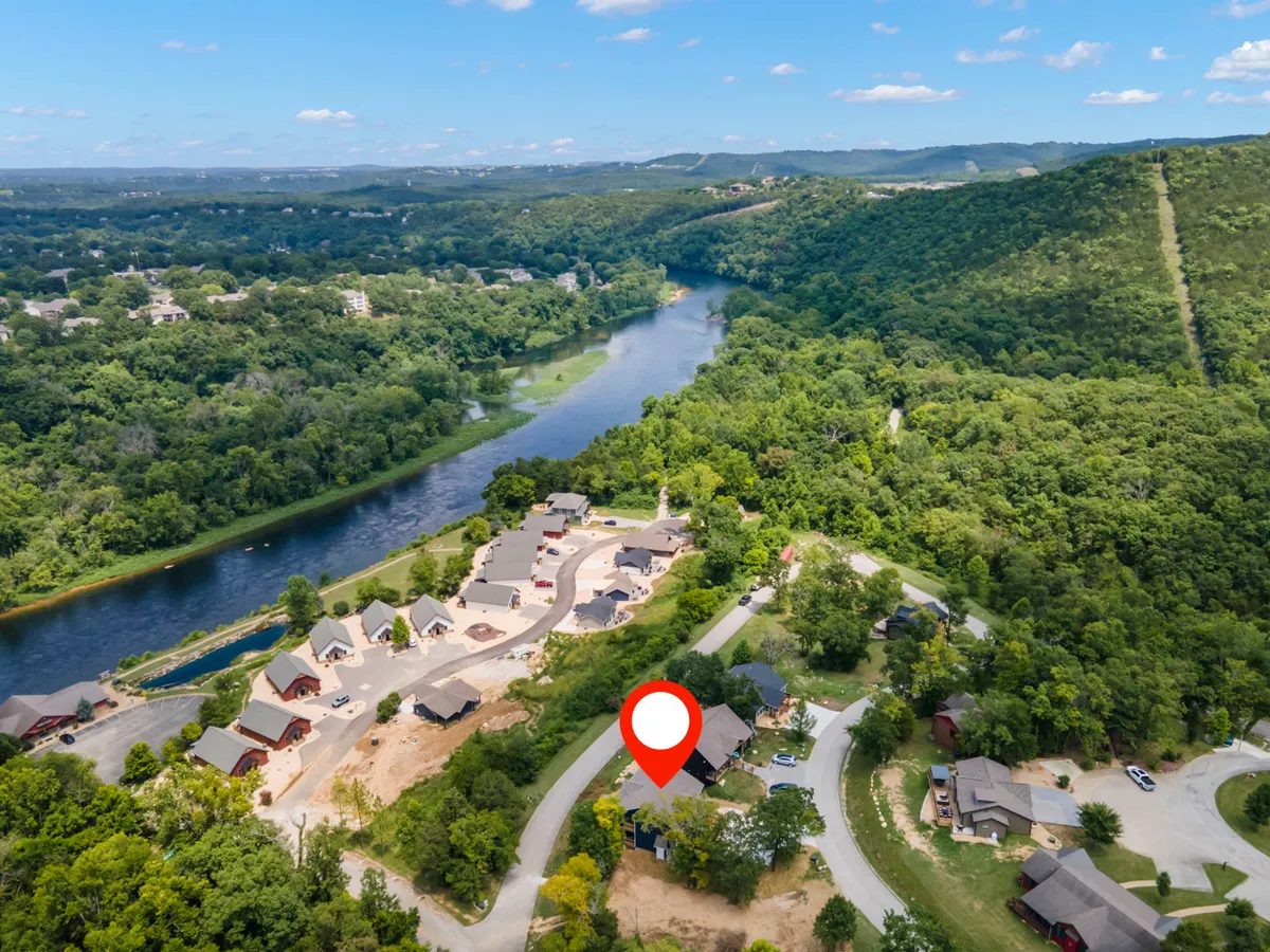 A sweeping view of the river winding through lush green hills, with residential buildings nestled along a curved road. The scene is tranquil, suggesting easy access to trails, water activities, and abundant wildlife.