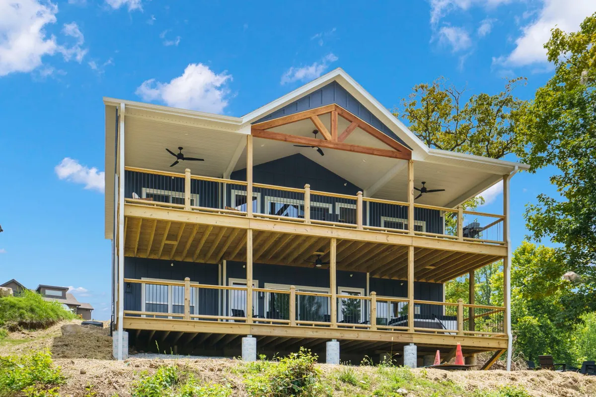 A wide-angle exterior view of a large wooden deck with prominent railings and a distinctive triangular roof, surrounded by greenery. The space is inviting for gatherings and offers a clear vantage point for sunset watching or stargazing.