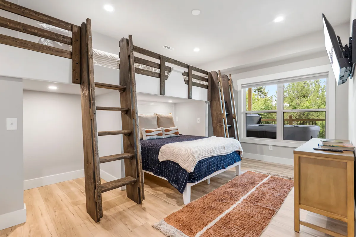 A playful, inviting lower-level bunk room with custom-built bunk beds, comfortable bedding, and a large window that brings in natural light. This room is designed for kids or teens, fostering a sense of adventure and comfort.